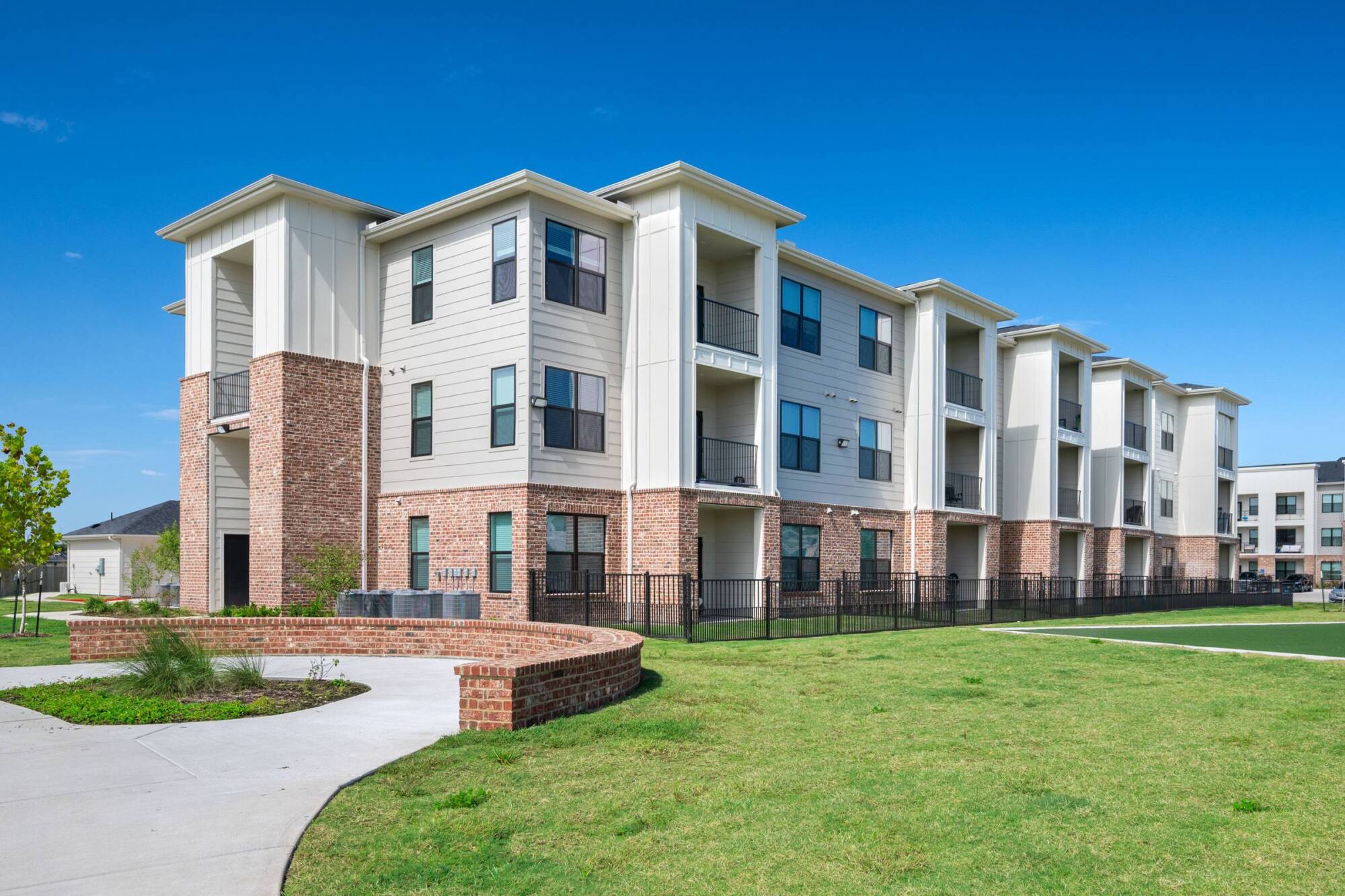 Building exterior at The Delta Pearland in Pearland, TX with brick and white siding, private balconies, and a landscaped lawn.